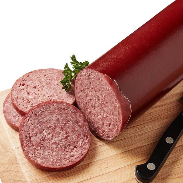 Sliced summer sausage in a red casing on a wooden cutting board